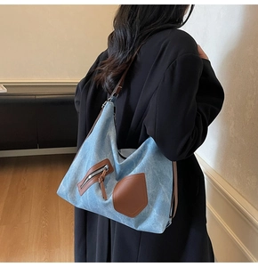 Close-up of light blue denim tote bag featuring brown leather trim and metal zipper pocket