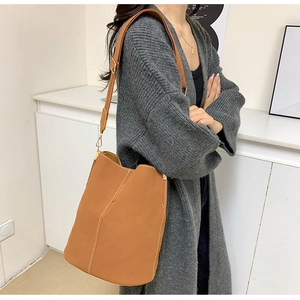 Detailed side view of a brown bucket bag with white contrast stitching and adjustable strap