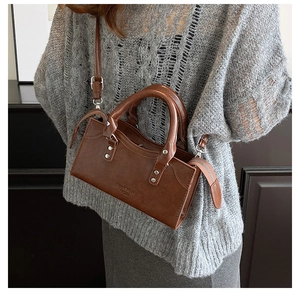 Detailed view of silver studs and embossed brand logo on a brown leather crossbody bag