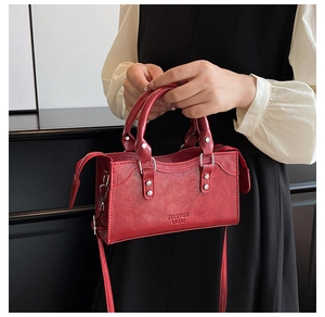 Detailed view of dark red PU leather handbag featuring silver rivets and zip closure