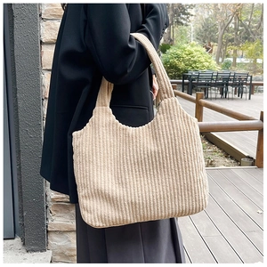 Vista lateral de un bolso tote de pana beige sobre un abrigo negro en un jardín