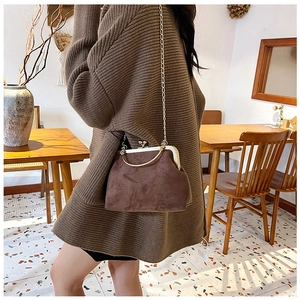 Sac boîte chic en daim marron foncé avec poignée dorée et chaîne porté par un modèle