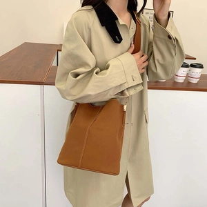 Caramel leather bucket bag with contrast stitching and wide shoulder strap on model