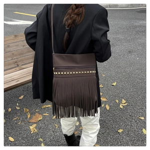 Detail of dark brown leather crossbody bag with golden studs and bohemian fringe tassels