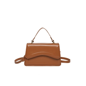 Brown faux leather crossbody bag with wavy flap and adjustable strap on white background