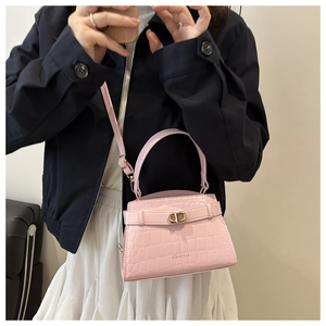 Detailed view of pink crocodile embossed handbag with golden clasp worn by a model