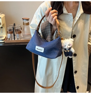 Detail of blue denim dumpling bag with brown leather handles and cute plush bear charm