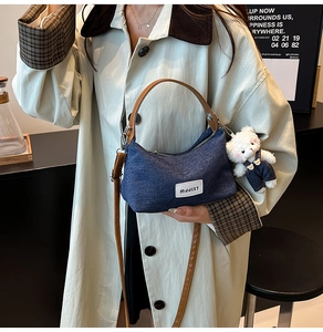 Detailed view of the denim dumpling bag with leather straps and a plush bear pendant