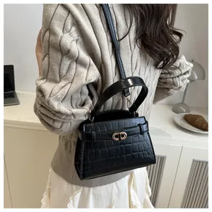 Detail of black crocodile texture crossbody bag with gold buckle on a stylish desk