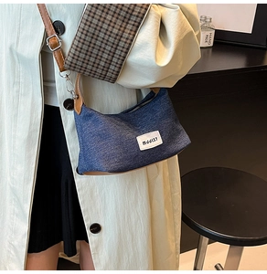 Detail of denim crossbody bag with brown leather strap and white woven label logo