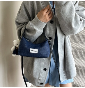 Detail of denim dumpling bag featuring black leather strap and a plush bear charm