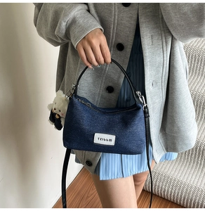 Detailed shot of dark blue denim hobo bag featuring white graphic patch and plush bear charm