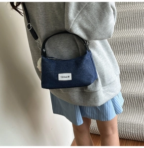 Side view of dark blue denim dumpling shoulder bag with plush pendant on a model