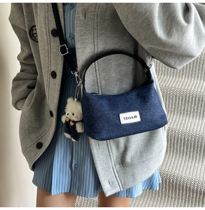 Close-up of denim hobo bag with white logo patch and cute plush bear keychain detail