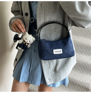 Detail of blue denim dumpling bag with black handle and a cute plush bear charm