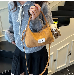 Brown suede dumpling bag with a cute bear charm and woven label detail on the front