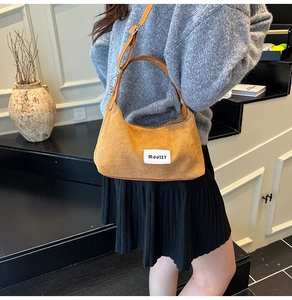 Close-up of brown suede crescent bag featuring a white logo tag and leather strap
