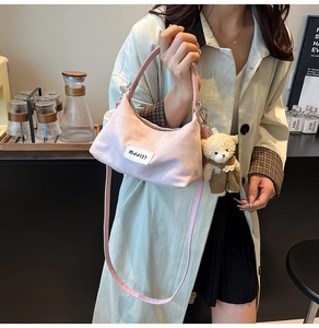 Detail of light pink corduroy half-moon bag with bear charm in cozy cafe setting