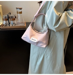 Detailed view of pink suede shoulder bag featuring white branded tag and metal zipper