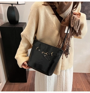 Detail of a shiny black bucket bag with a golden horsebit buckle worn by a model