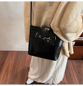 Close-up of a glossy black shoulder bag with gold buckles worn by a model in soft lighting