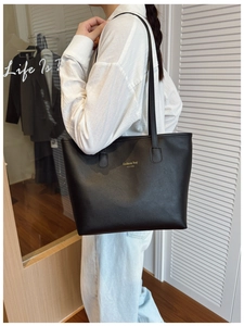 Detalle del bolso tote negro grande con letras doradas llevado al hombro en tienda