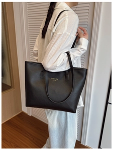 Detalle del bolso tote grande de cuero negro con letras doradas en el hombro de una modelo