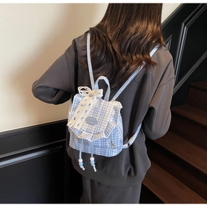 Close-up of blue plaid backpack featuring white lace bow and beaded drawstring detail