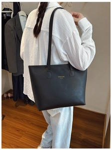 Detalle del bolso tote de cuero negro con letras doradas en un entorno de interior