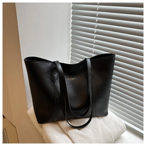 Close-up of black leather tote bag with gold stamped text on textured white fabric