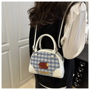 Close-up of blue gingham crossbody bag with red apple print worn by a female model