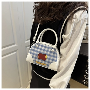 Detail of blue plaid crossbody bag with apple print and white faux leather handles