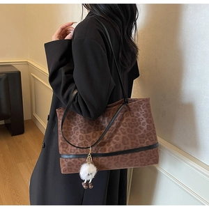 Detail of leopard print tote bag with black leather straps and white pom-pom charm