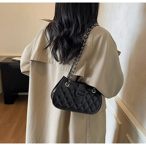 Dettaglio borsa trapuntata nera con catena dorata indossata su un trench beige classico