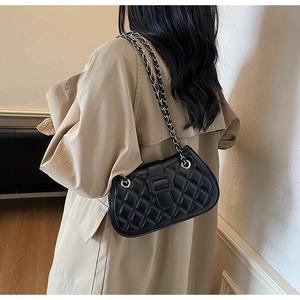 Detail of black quilted shoulder bag featuring gold chain strap and square buckle