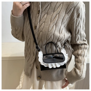 Close-up of black leather mini bag featuring white lace trim and bow detail