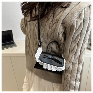Close-up of black crossbody bag with white lace trim and bow on model's beige sweater outfit