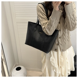 Detail of elegant black leather tote bag featuring gold embossed logo on the surface