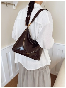 Detailed close-up of glossy brown faux leather texture and gold metal buckle on tote bag