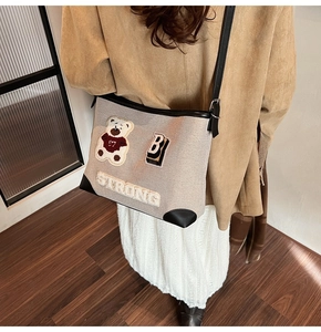 Dettaglio della borsa in tela beige con ricamo orsetto, scritta Strong e manici in pelle