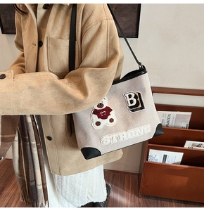 Dettaglio borsa tote in tela con patch orsetto, ricamo e rifiniture in pelle nera