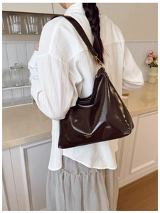 Detail of dark brown glossy patent leather hobo bag with gold logo and wide shoulder strap