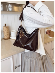 Close-up of dark brown glossy leather tote bag with gold hardware and creative charms