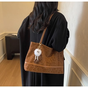 Detail of leopard print canvas tote bag with leather straps and plush charm on black coat