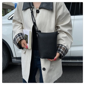 Nahaufnahme der schwarzen Leder-Eimertasche mit Logo vor einem beigen Mantel Outfit