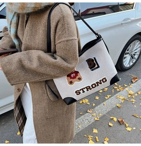 Dettaglio della borsa in tela beige con orsetto 3D, patch STRONG e tracolla in pelle