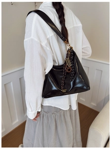 Detailed back view of a black glossy leather tote bag with stylish charms on a model