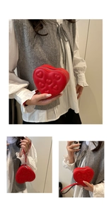 Detail of red heart-shaped clutch bag with embossed patterns and wrist strap
