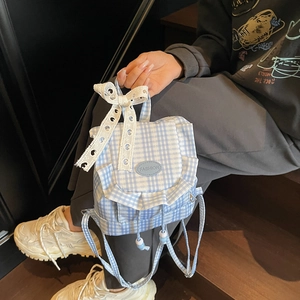 Blue gingham backpack with white lace bow and ruffled edges in a stylish outdoor setting