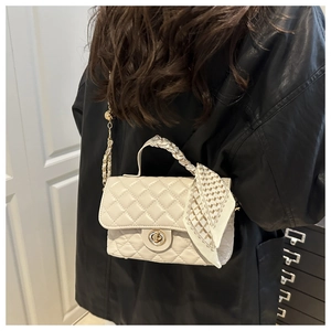 Detail of cream quilted handbag featuring a metal twist lock and silk scarf handle detail
